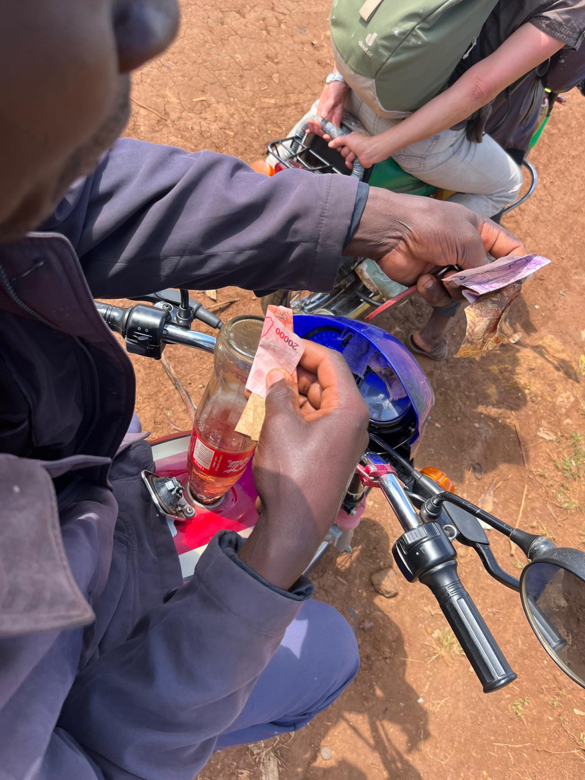 Refuelling a boda-boda motorcycle at a roadside vendor in rural Uganda — petrol sold from a cola bottle