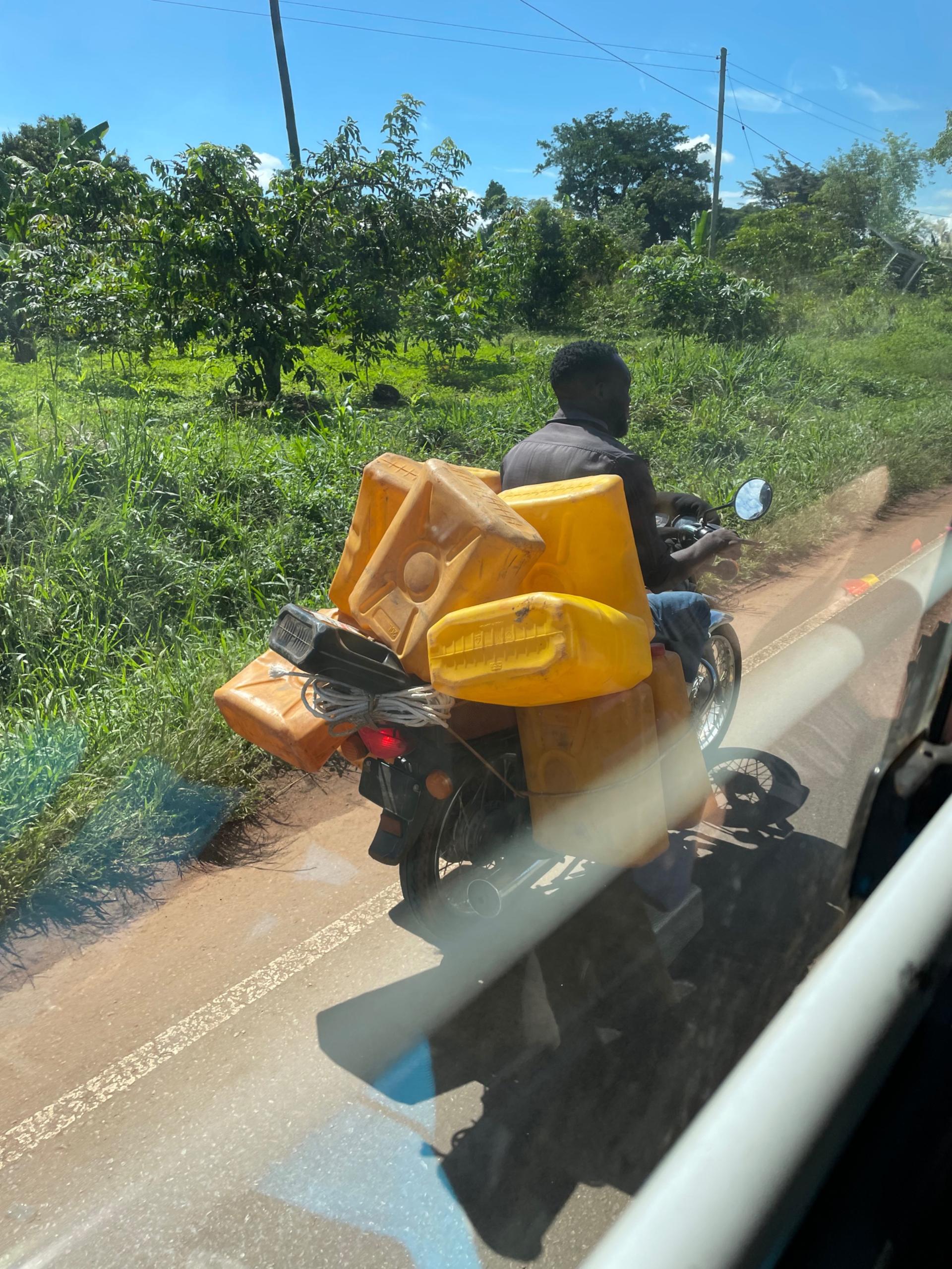 Boda-boda driver carrying multiple yellow water jerrycans on a rural road in Uganda